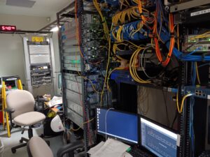 Control room with equipment for a Mitel Phone System, multiple computer screens and walls of wires